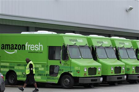 A worker walks past Amazon Fresh delivery vans parked at an Amazon Fresh warehouse in Inglewood